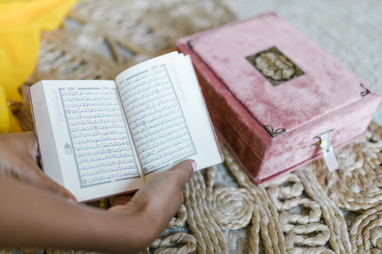 A person holding an open Quran for prayer next to a pink box. Islamic faith and devotion.